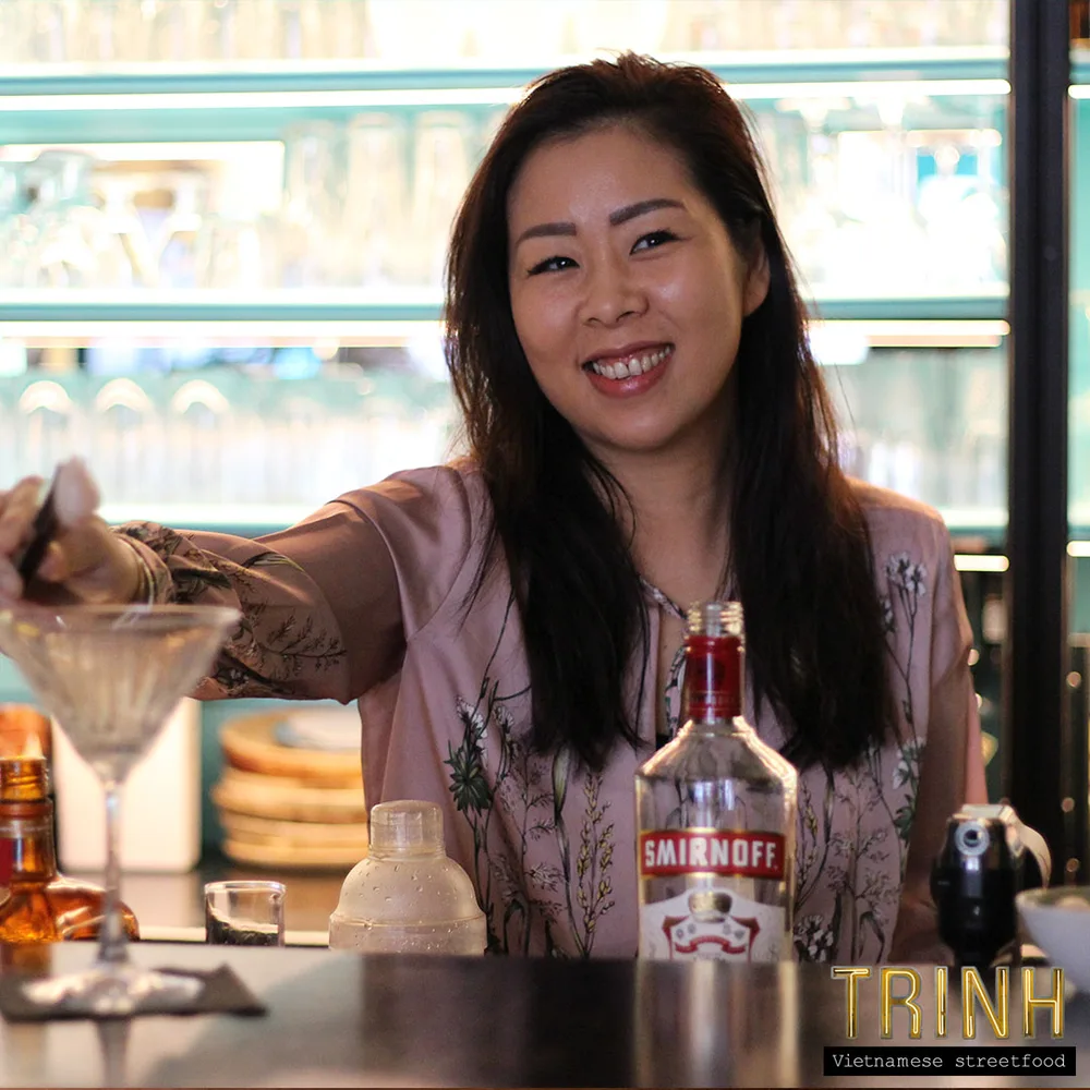 Vrouw achter de bar schenkt een cocktail in, flessen op de bar.