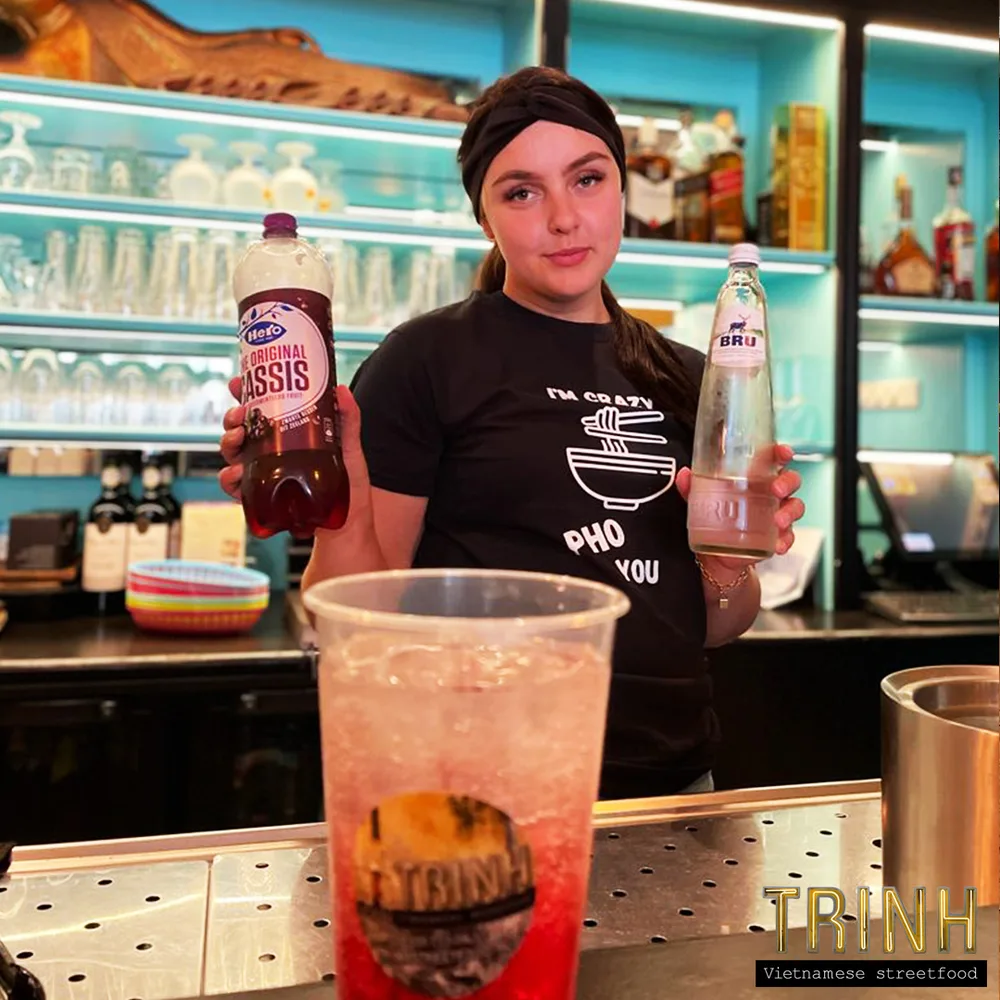 Medewerkster achter de bar houdt twee flesjes frisdrank vast naast een glas ijsthee.