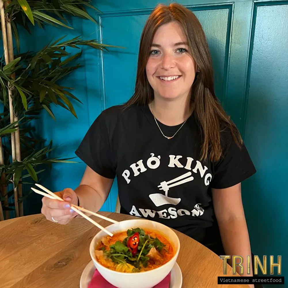 Gast met een "Phở King Awesome"-shirt eet een kom currynoedelsoep.