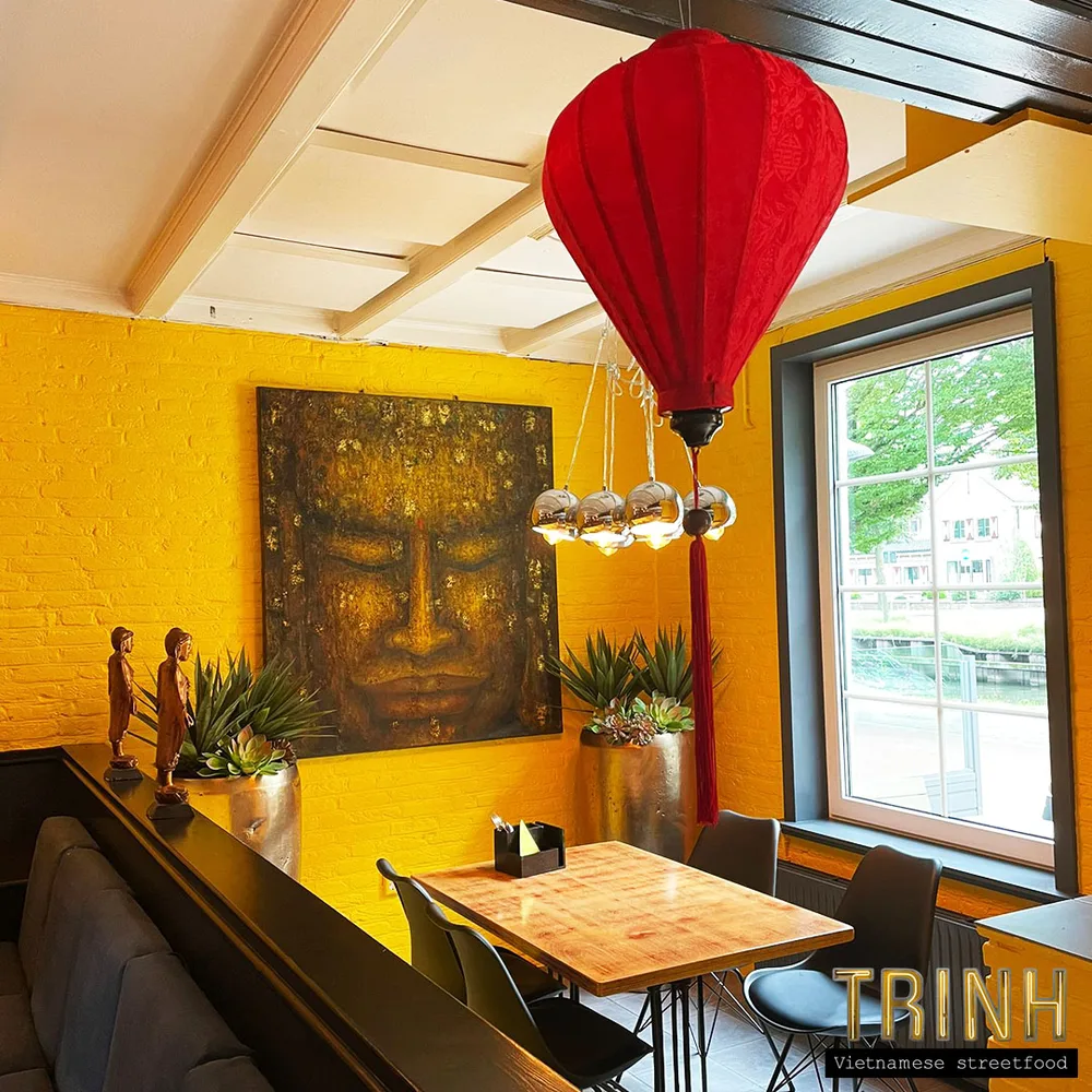 Zithoek met een rode Vietnamese lampion, een boeddhaschilderij en een gele muur.