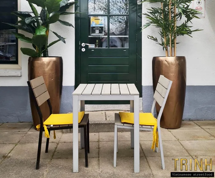 Terrastafel met twee stoelen met gele kussens naast de groene voordeur van het restaurant.