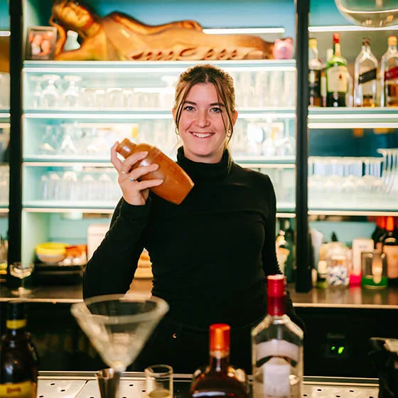 Medewerkster achter de bar met een cocktailshaker, flessen op de achtergrond.
