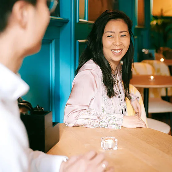 Lachende vrouw aan tafel in gesprek met een gast in het restaurant.