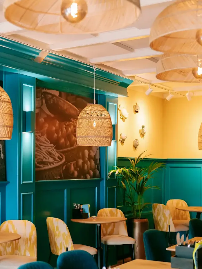 Eetzaal met turquoise lambrisering, een gele muur, rotan hanglampen en planten.