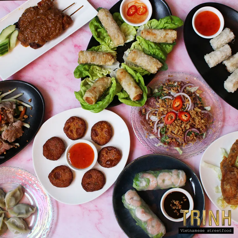 Tafel vol Vietnamese deelgerechten van bovenaf: loempia's, saté, viskoekjes, gỏi cuốn en salade.