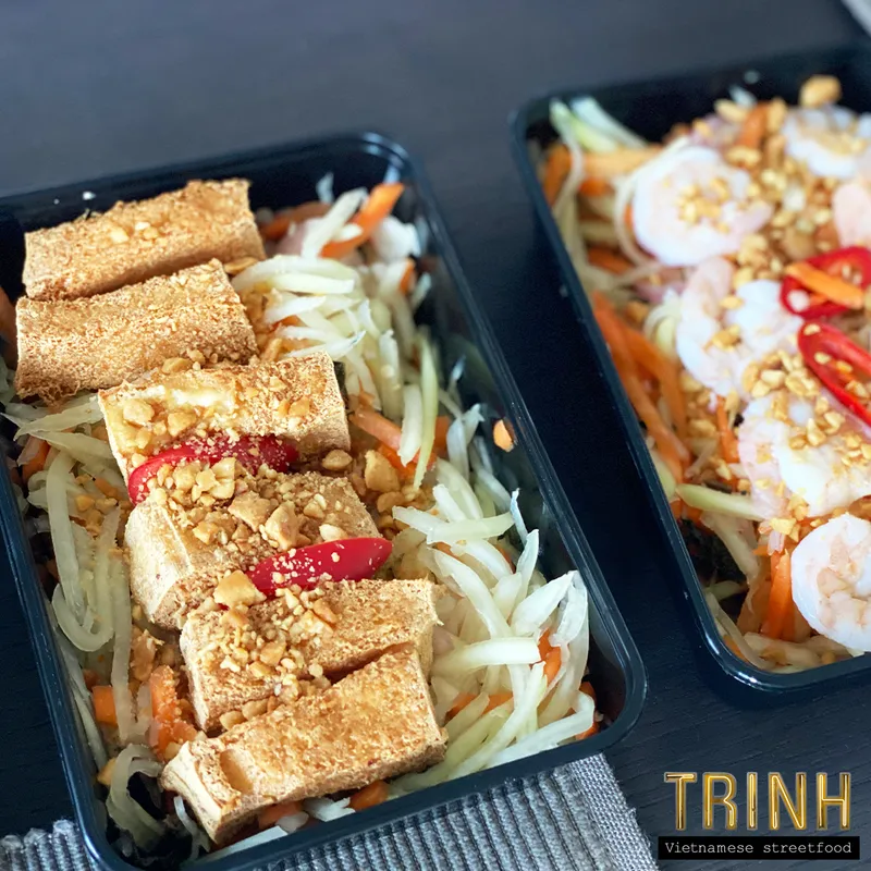 Twee afhaalbakjes met gỏi đu đủ — groene papajasalade met tofu en pinda's.