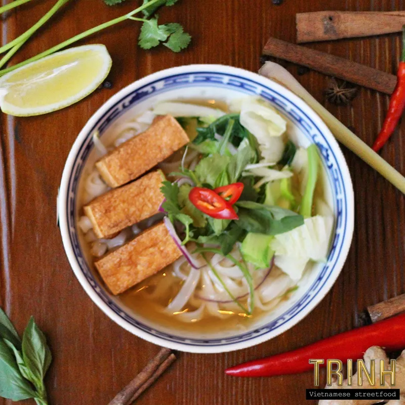 Kom phở met gefrituurde tofu, taugé en verse kruiden, van bovenaf, tussen kaneelstokjes, steranijs en rode pepers.