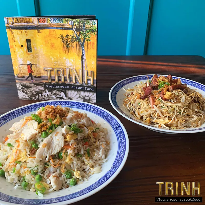 Menuboekje van Trinh naast een bord gebakken rijst en een bord gebakken mie.
