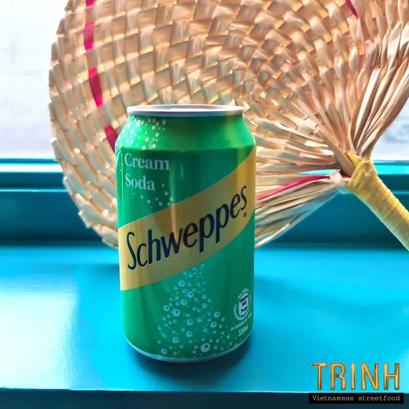 Blikje Schweppes Cream Soda voor een gevlochten waaier op een turquoise vensterbank.