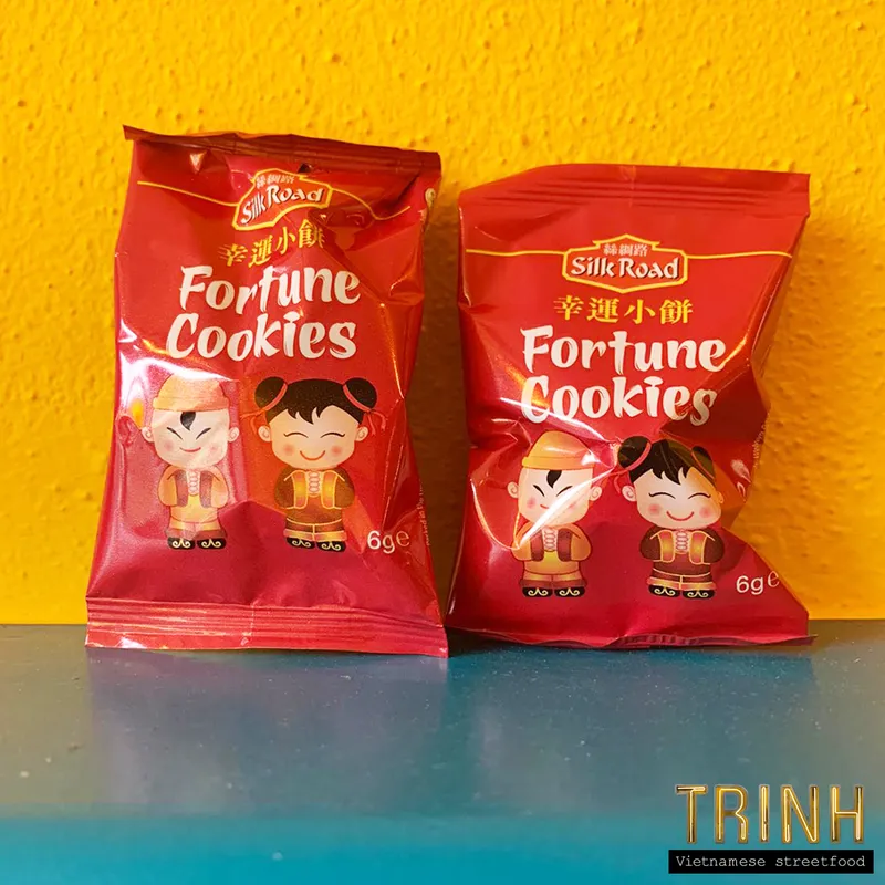 Twee zakjes fortune cookies tegen een gele muur.