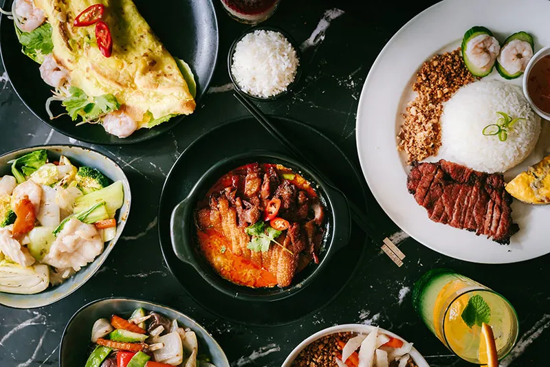 Meerdere gerechten van bovenaf op een donkere tafel: rijst, curry, gewokte groenten en salade.
