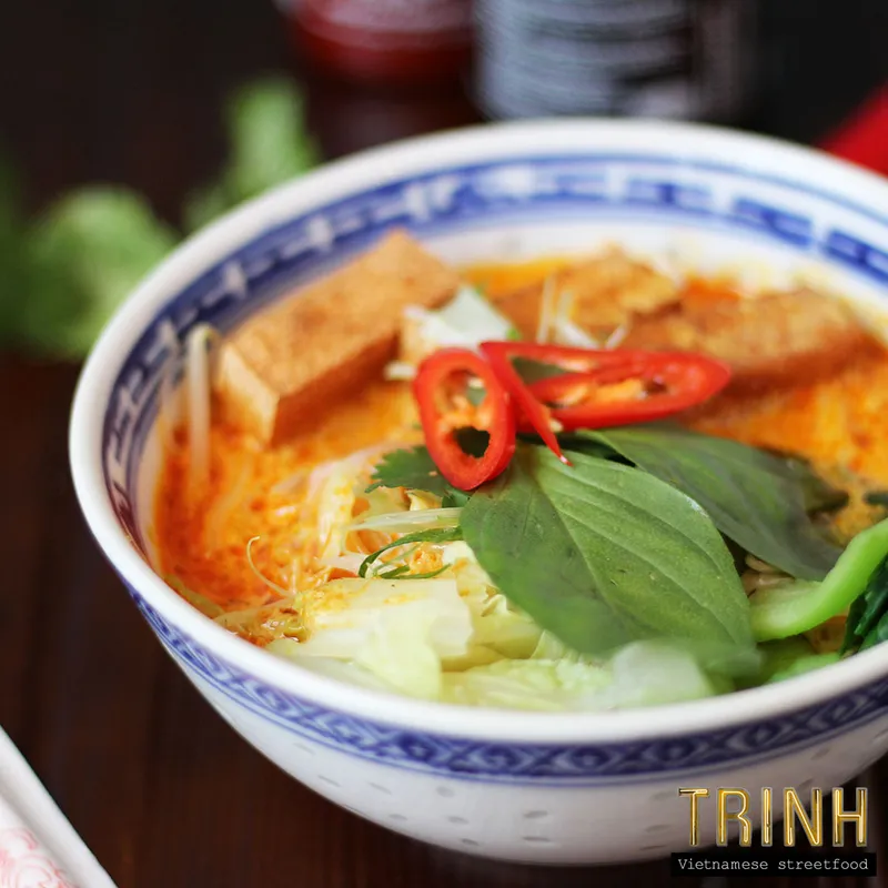 Kom pittige currynoedelsoep met gefrituurde tofu, rode peper en Thaise basilicum in blauw-wit porselein.