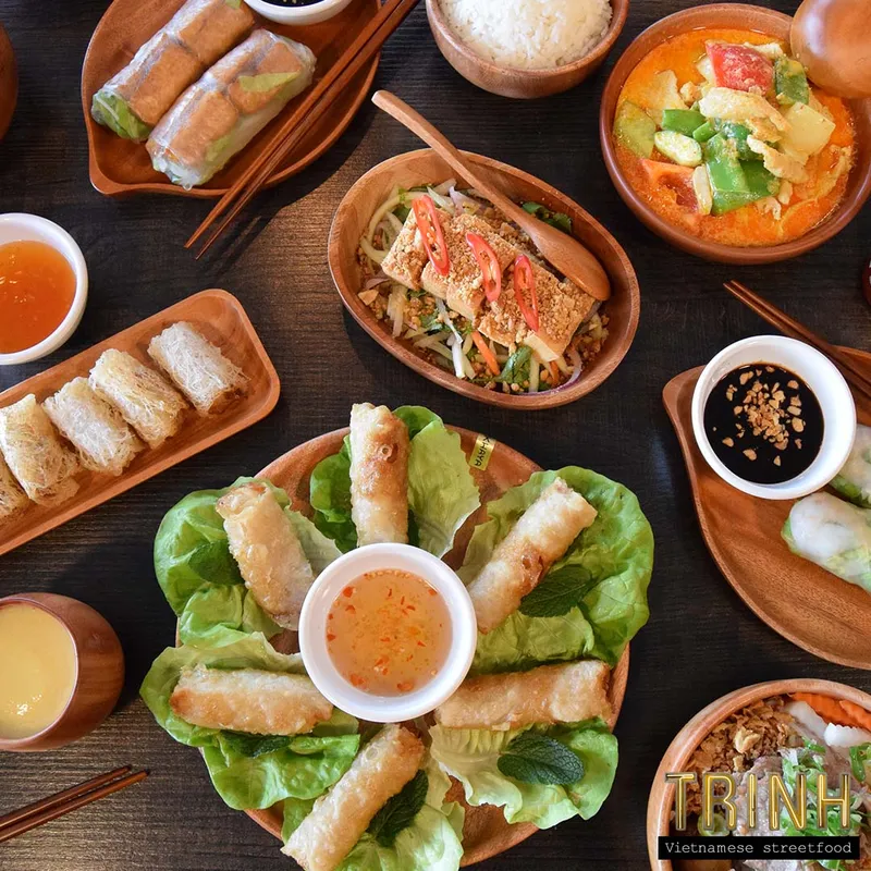 Gedekte tafel van bovenaf met loempia's, gỏi cuốn, curry, rijst en dipsausjes.