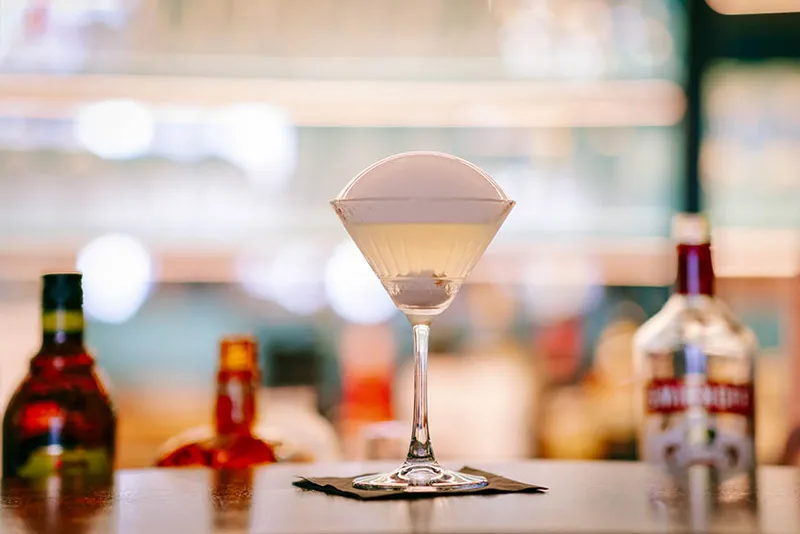Cocktail in een coupeglas op de bar, flessen wazig op de achtergrond.