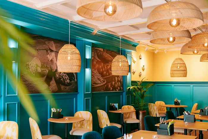 Restaurantinterieur met turquoise lambrisering, rotan hanglampen en een gele muur.