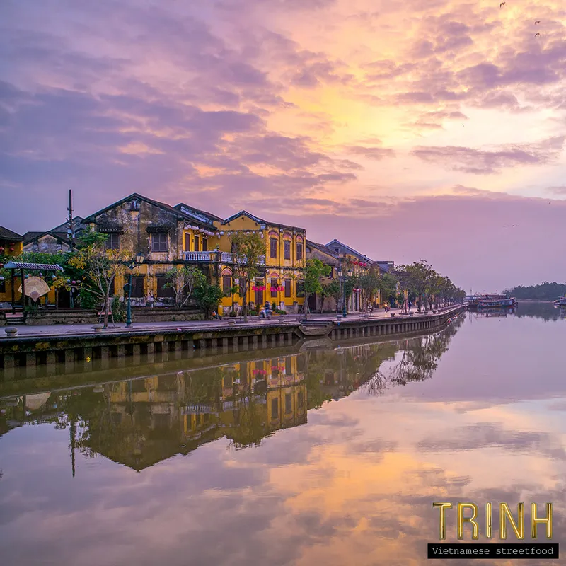 De rivier van Hội An bij zonsondergang met historische gevels weerspiegeld in het water.