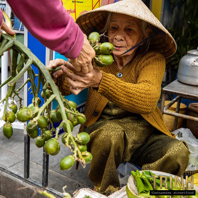 Oudere marktvrouw met kegelhoed verkoopt groente op straat in Vietnam.