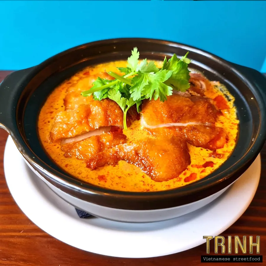 Kleipot met pittige kipcurry en koriander tegen een turquoise achtergrond.